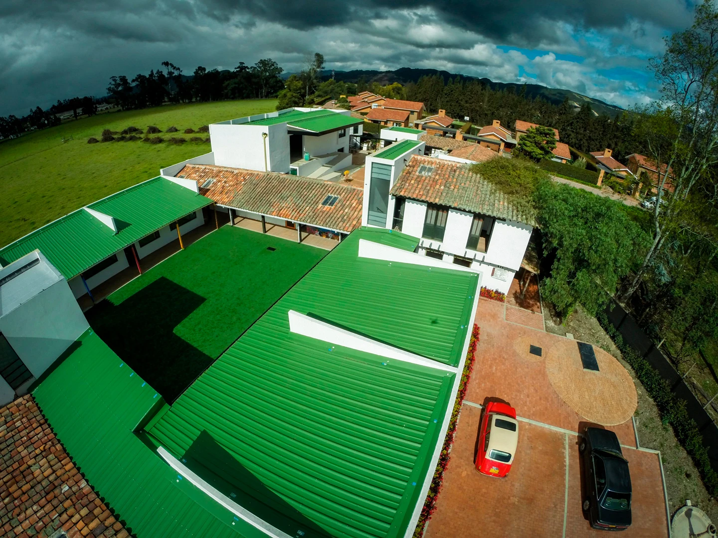 Patio central y aulas del Colegio Alemán en Cajicá con cubiertas metálicas verdes y zona de parqueaderos